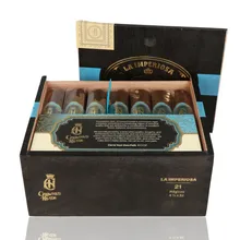 Open black wooden box of 21 Crowned Heads La Imperiosa Magicos cigars, showing seven individually sleeved dark brown cigars across the front row with ornate turquoise and gold Crowned Heads bands.