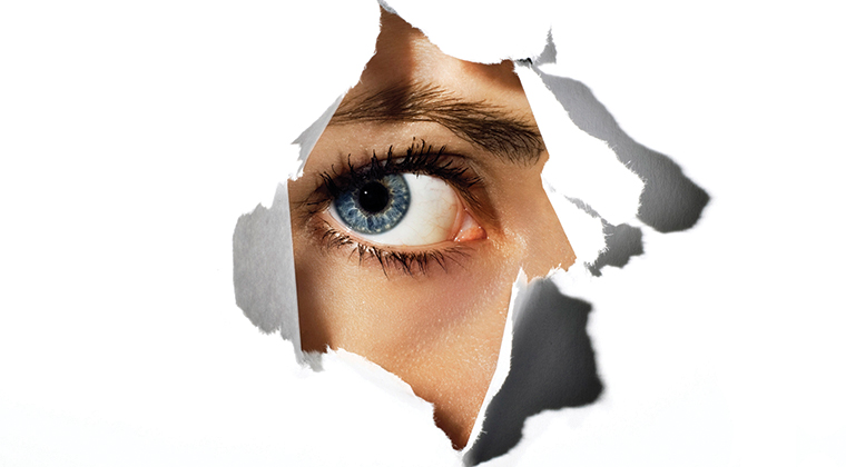 an eye peeking throw a hole in the paper