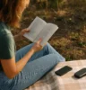 Person enjoying nature or reading a book outdoors with phone turned off and placed face down nearby.