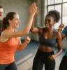 Diverse group of people in a high-energy group fitness class (e.g., HIIT, spin, bootcamp) smiling, moving in sync, or high-fiving post-workout