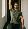Athlete performing overhead kettlebell carry, walking in gym corridor, focused expression, strong posture, natural light highlighting shoulder and core engagement