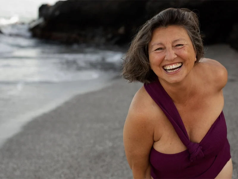 Happy senior woman in purple swimsuit laughing on the beach