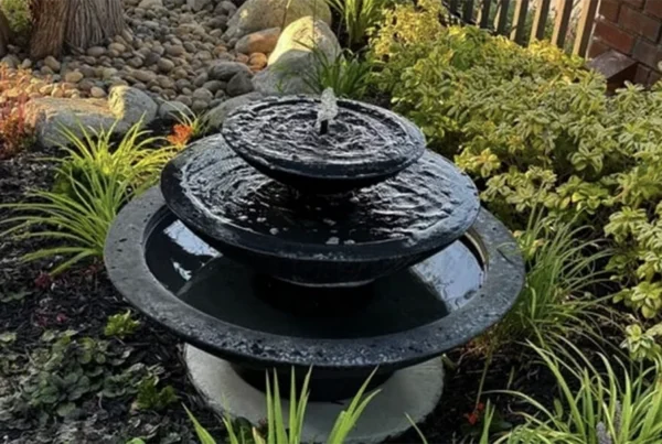 Three-tier black stone water fountain in a lush garden