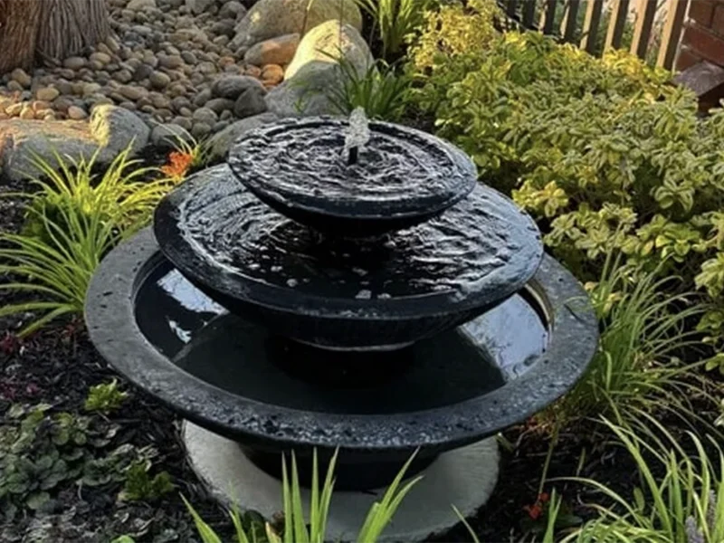 Three-tier black stone water fountain in a lush garden