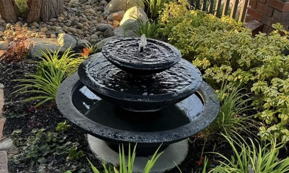 Three-tier black stone water fountain in a lush garden