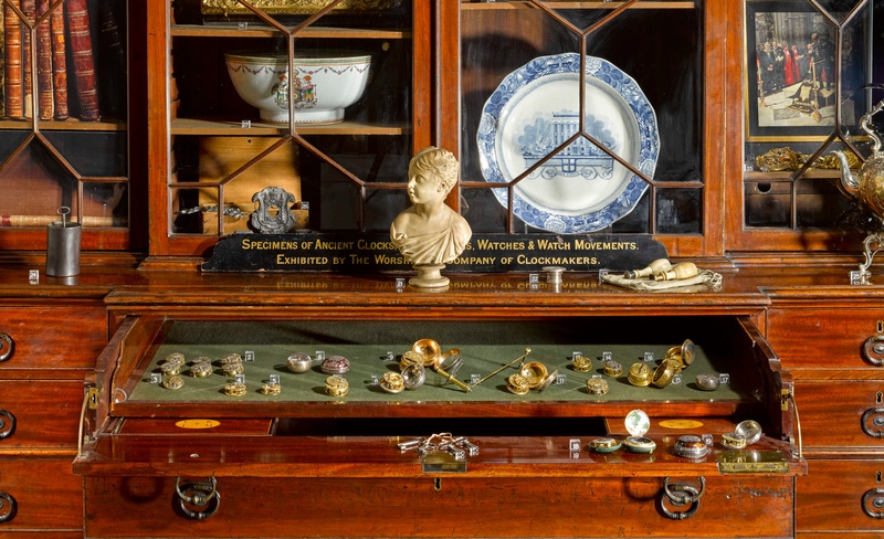 A close up of a cabinet with an open drawer covered in watches and various items stored in the glazed bookcase