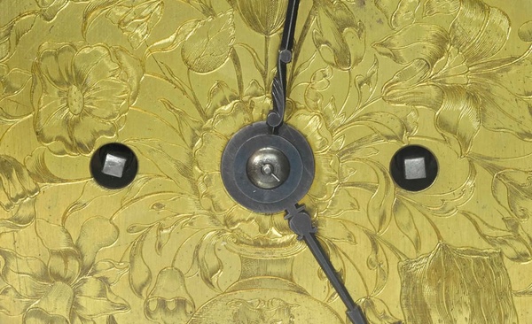 a close up of a clock dial showing the winding holes, clock hands and engraving 