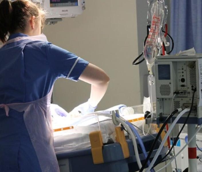 Nurse with her back to camera looking after a baby in a cot, surrounded by lots of medical equipment