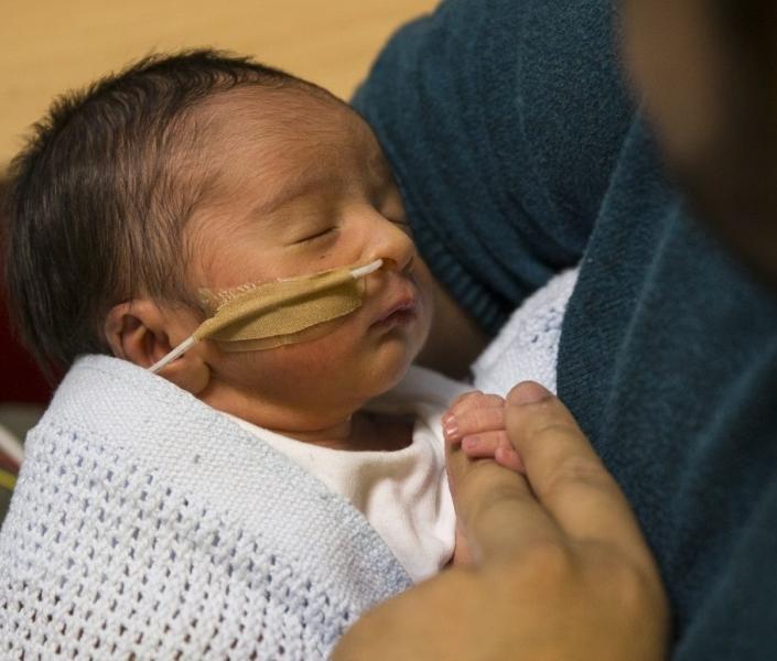 Baby in neonatal care being held by his father