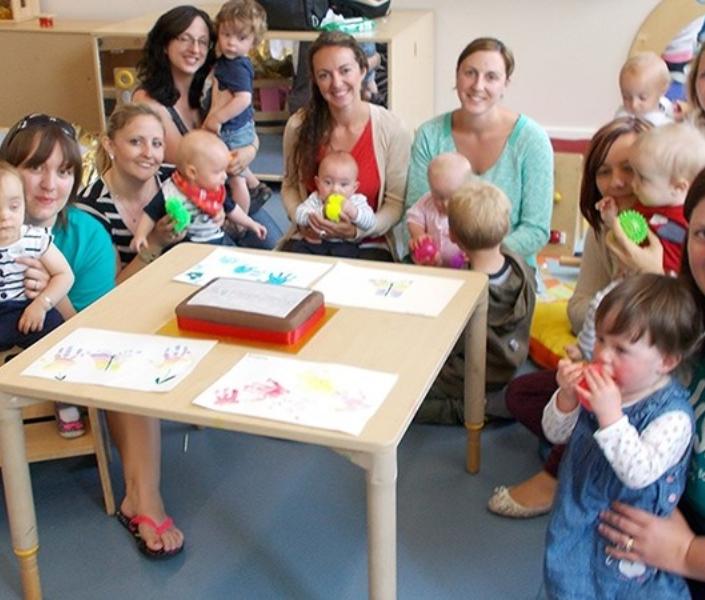 Group of mums and babies with Bliss volunteers sitting around a table in a play area