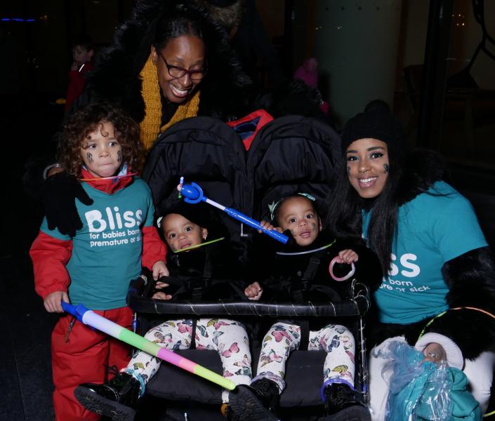 2 Adults, young child and 2 toddlers in a twin buggy wrapped up warm in darkness