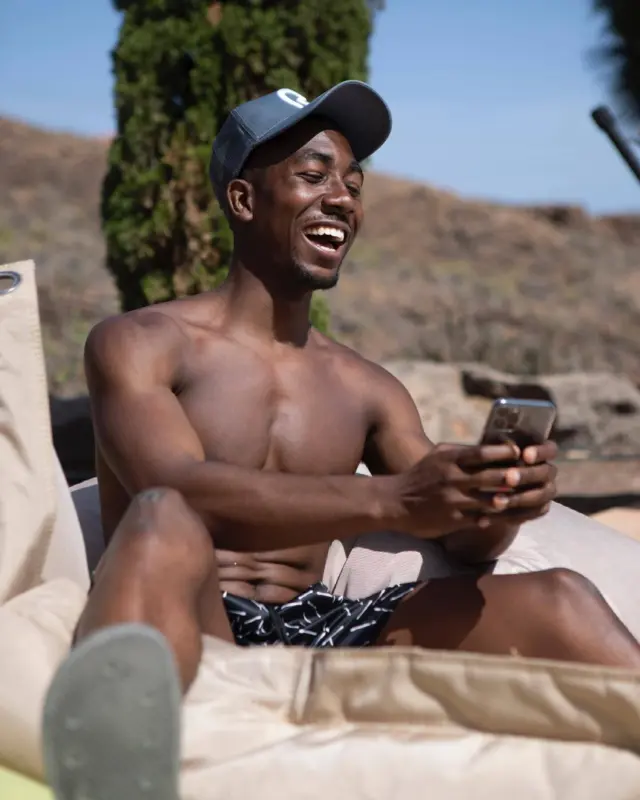 A man laughing at his phone by a pool