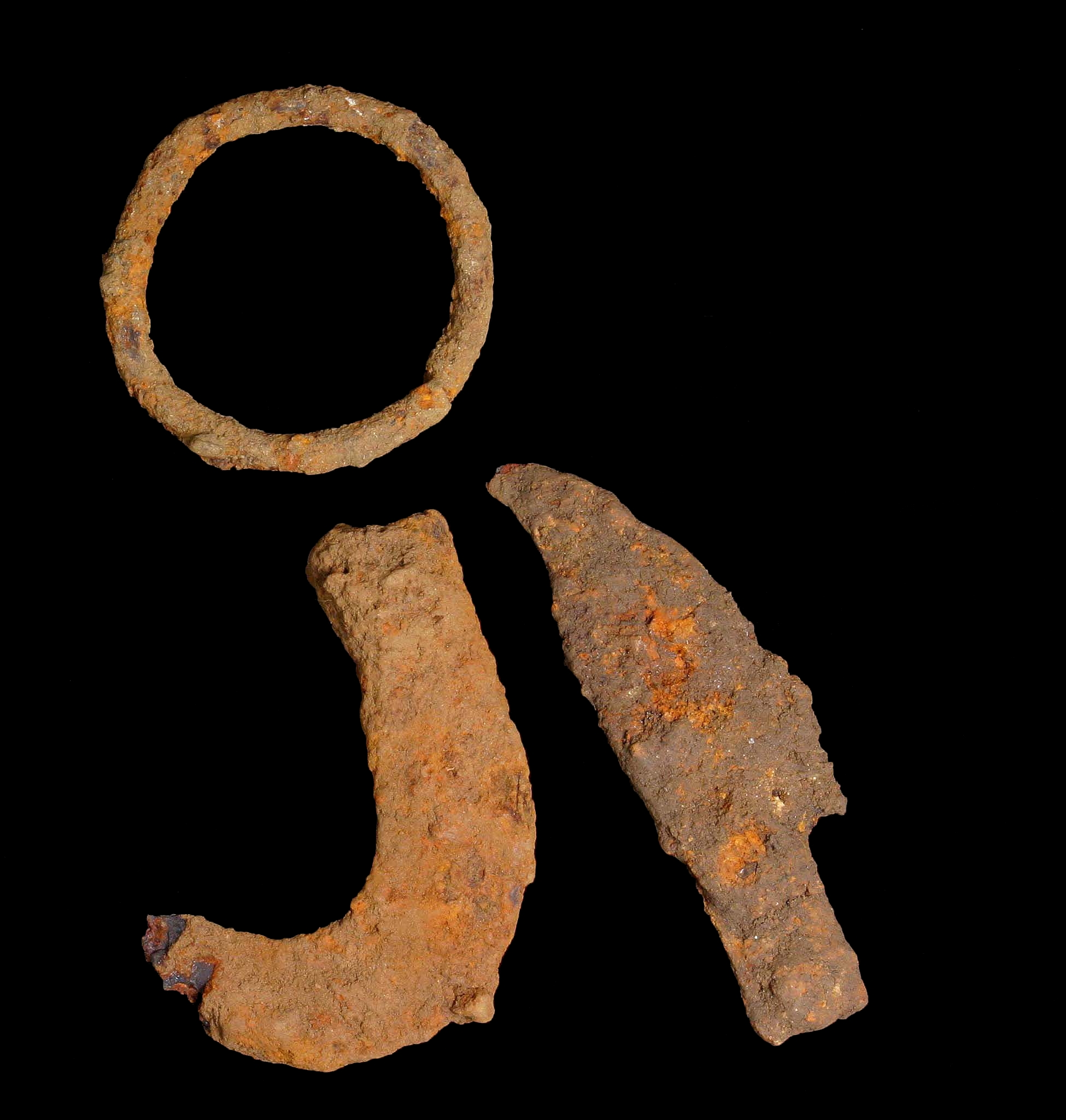 Iron Age sickle blade, knife blade and iron ring arranged on a black background