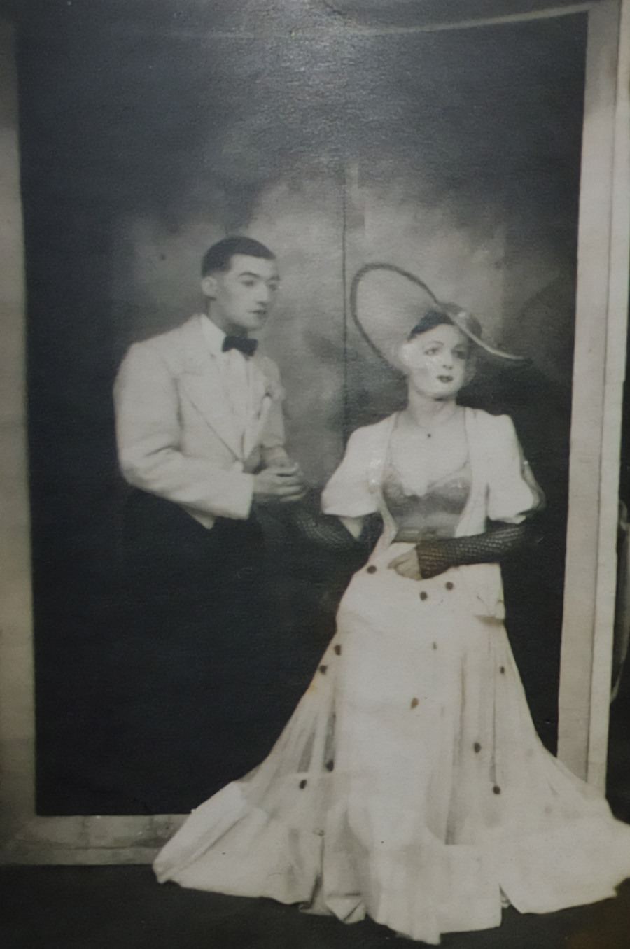 Two male prisoners in costume on a small stage, one in a white evening suit and the other dressed as a woman in a long gown and wide hat.