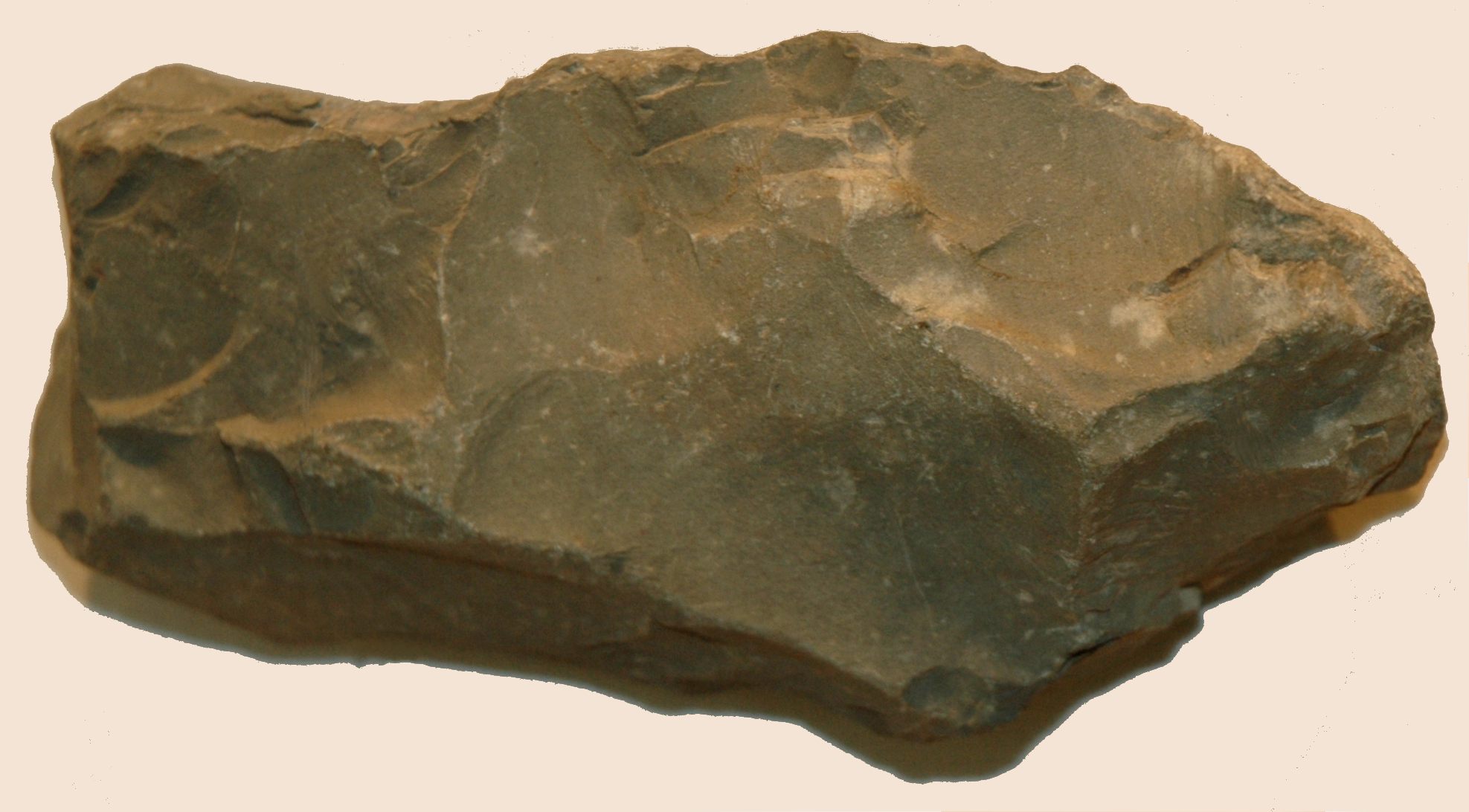 Stone axe head made of polished stone, showing flaked edges and a roughly triangular shape. The surface has visible chips and irregularities.