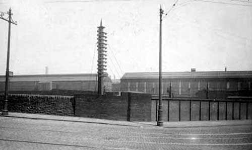 A view of Leeds Forge from Armley Road, showing long, low buildings behind a brick wall.