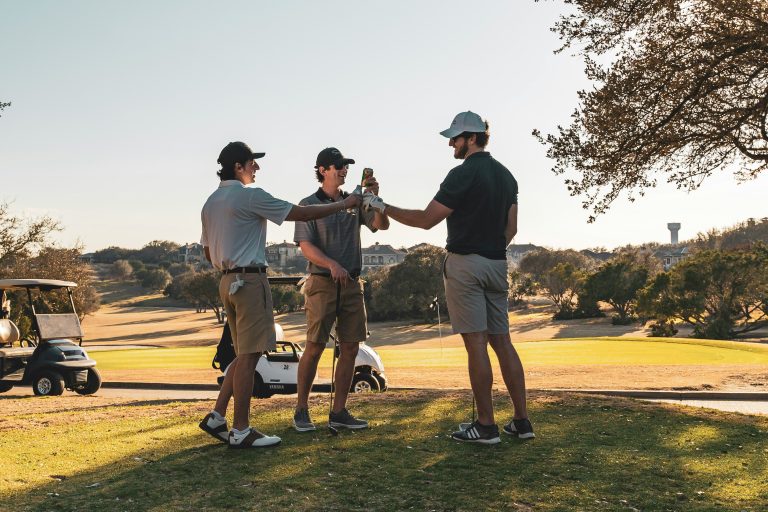 Group of golfers toasting with drinks on golf course at sunset
