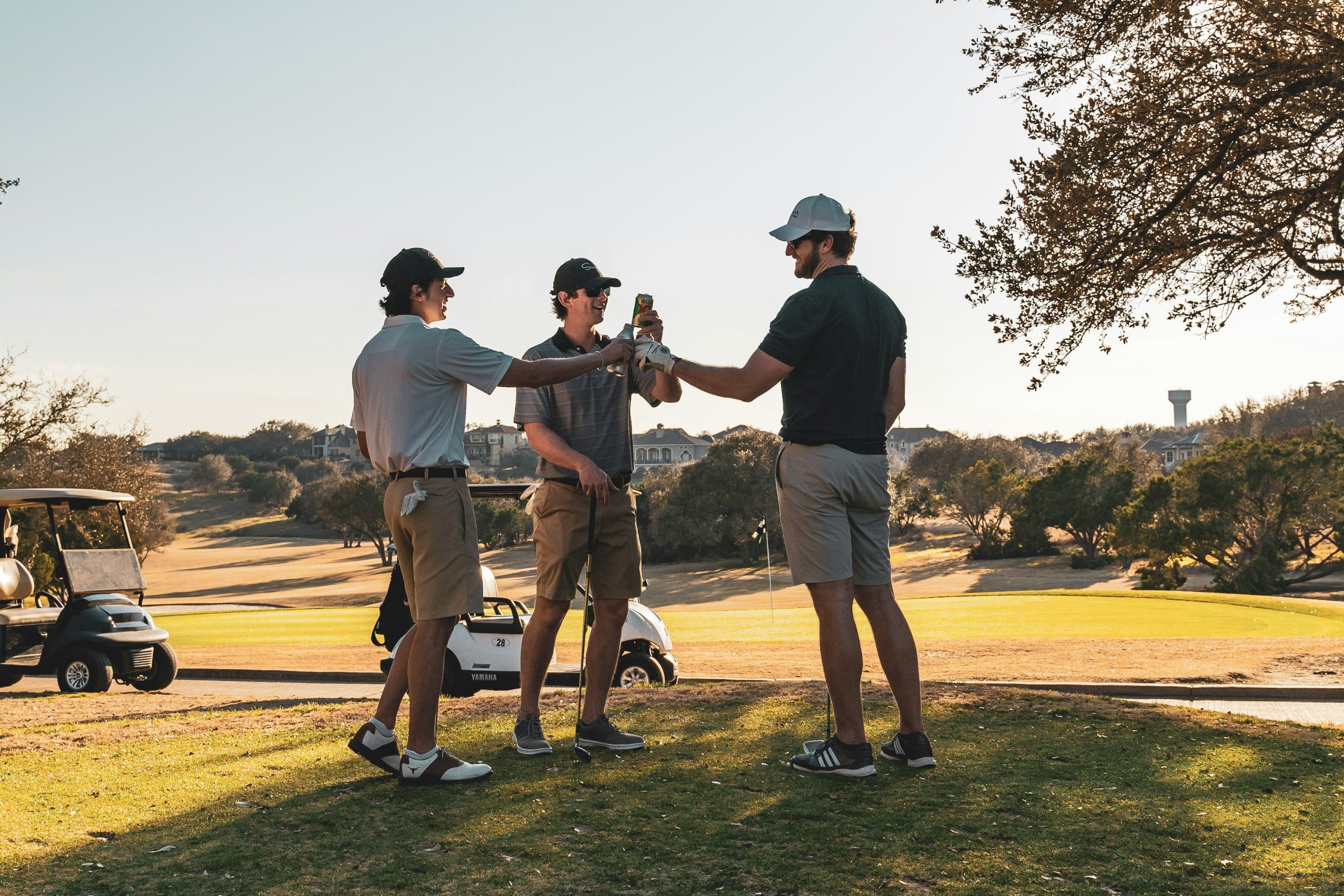 Group of golfers toasting with drinks on golf course at sunset