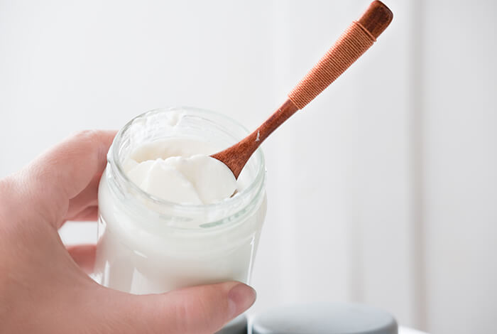a jar of Greek yogurt held in one hand with a wooden spoon inside