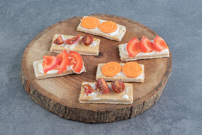 sliced bread topped with tomato and carrot on a wooden board
