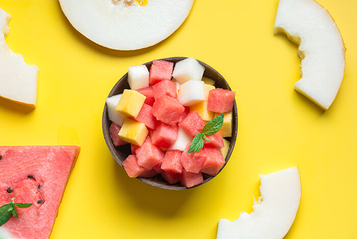 bowl of mixed watermelon and cheese cubes on a yellow background with scattered melon slices