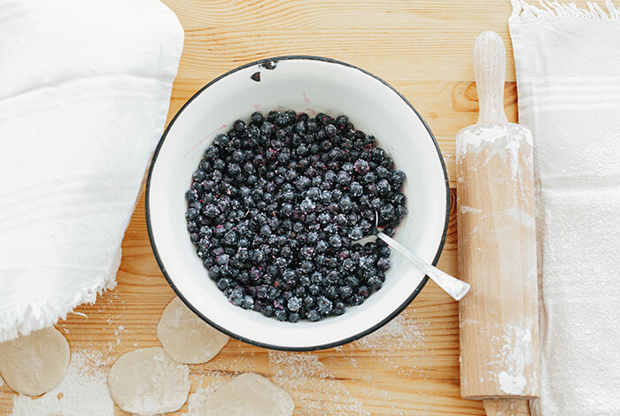 fresh blueberries in a white bowl and a rolling pin next to it