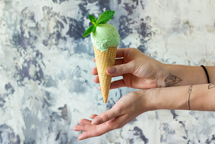 a hand holding a mint-flavored ice cream topped with fresh mint leaves