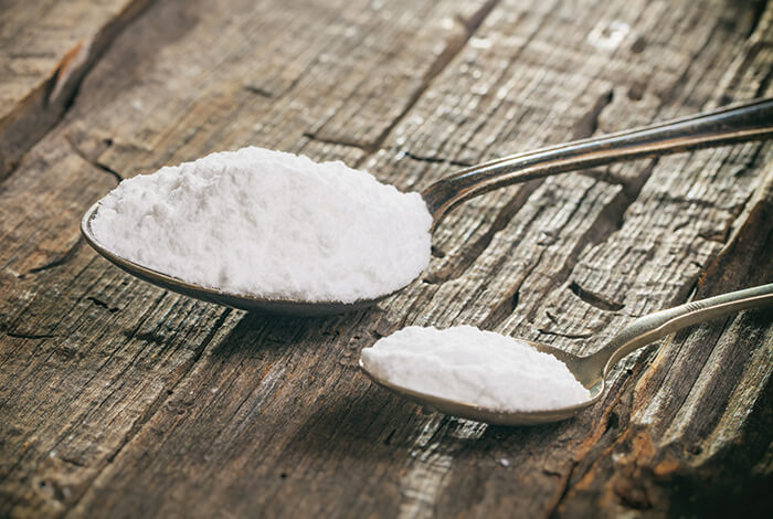 two spoons filled with baking soda on a wooden surface