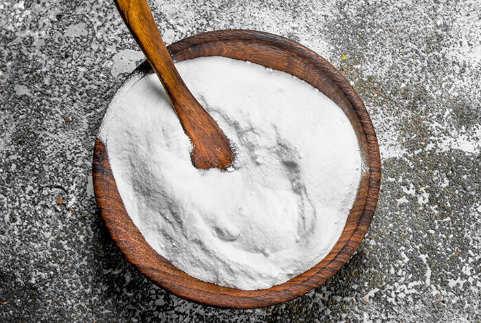 a bowl of white baking soda powder with a wooden spoon inside