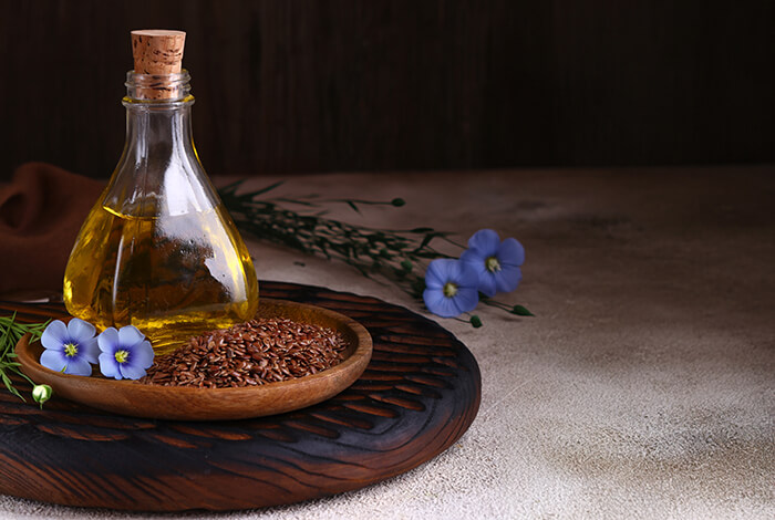 a glass bottle of golden flaxseed oil on a wooden plate, surrounded by whole flaxseeds