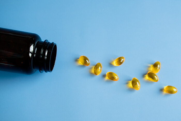 a dark bottle spilling fish oil gel capsules onto a blue background