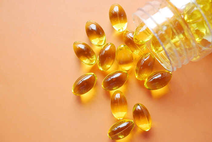 a clear bottle tipped over, spilling fish oil gel capsules onto an orange surface