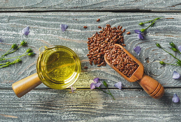 a glass jar of golden flaxseed oil with a wooden scoop of flaxseeds on a rustic wooden surface