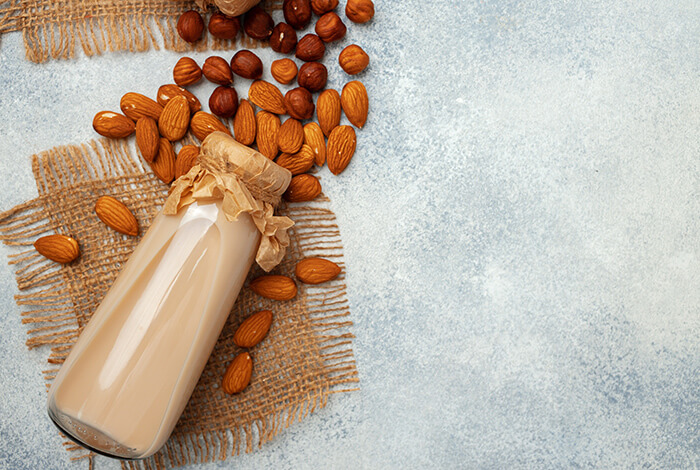 a glass bottle of almond milk on burlap, surrounded by almonds 
