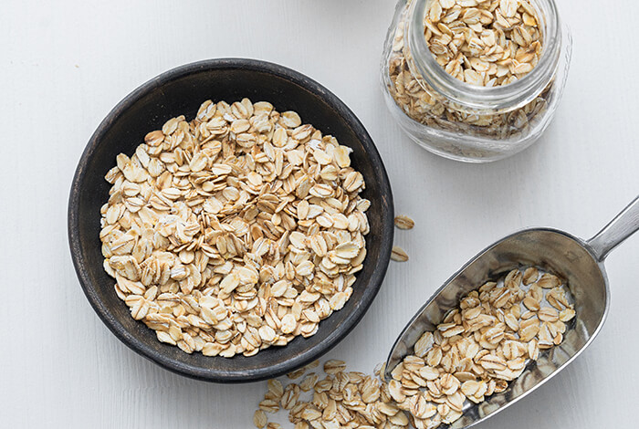 dried oats in a bowl, in a jar, and a stainless scooper