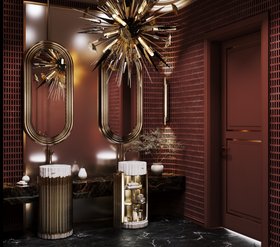 Bathroom | deep red paint luxury bathroom in dark marble finishes with Symphony white pedestal sink and cabinet for storage, Colosseum curvy gold wall mirror, Outburst chandelier, Cyrus wall lamp, and vase