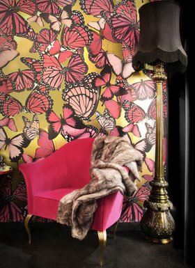 Living Room | glamorous reading corner in art deco style with Mimi curvy pink armchair, Lotus dark and gold floor lamp, butterfly wallpaper, and blanket