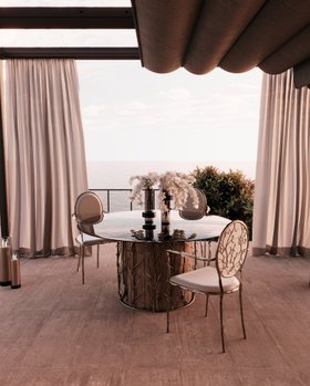 Outdoor | balcony dining area in nature-inspired style with Enchanted smoked glass and brown wood dining table, Enchanted white dining chair, vase, curtain, and wood flooring
