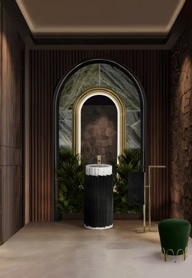 Bathroom | nature-inspired bathroom in brown wood and marble finishes with Symphony dark pedestal sink, Colosseum curvy gold wall mirror, Eden towel rack, Nui deep green stool, floral ornaments, and lavish flooring