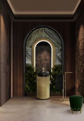Bathroom | nature-inspired bathroom in brown wood and marble finishes with Symphony gold pedestal sink, Colosseum curvy wall mirror, Eden towel rack, Nui deep green stool, floral ornaments, and lavish flooring
