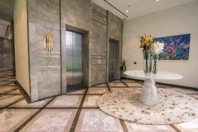 An Upscale Apartment in India | access hall with Pietra white marble table, Oslo terrazzo rug, Brubeck retro gold wall lamp, floral wall art, vase, elevator, and marble flooring