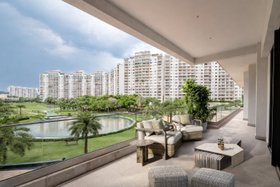 An Upscale Apartment in India | balcony area with Hampton wood and rattan armchair, Mayer white marble center table, side table, puff, cushion, and stone flooring