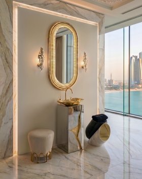 Bathroom | luxury bathroom in gold and white tones with Lapiaz glass cabinet for storage, Lapiaz vessel sink, Colosseum wall mirror, Nui cosy stool, Jacobsen retro side table, Cay wall lamp, and marble flooring