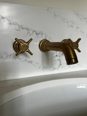 Swadling Illustrious Wall Mounted Basin Mixer with Curved Spout and Brushed Brass finish against marble tiles