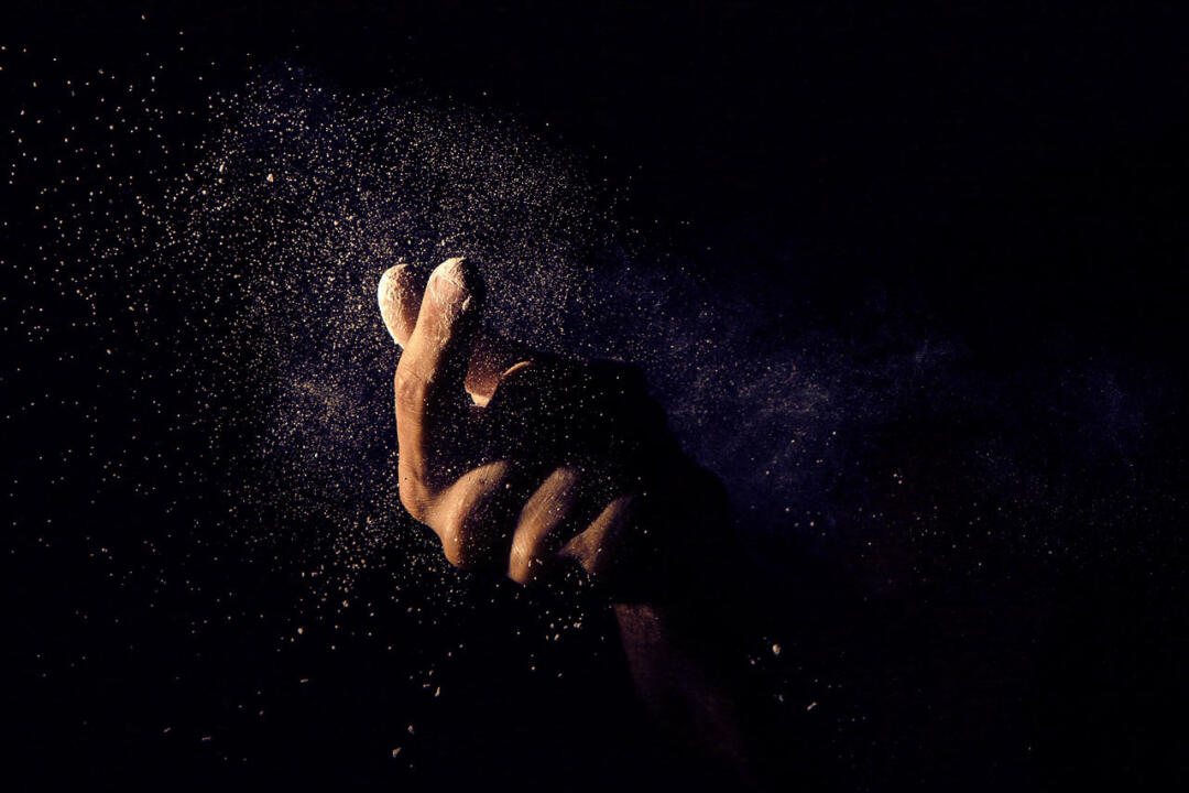 A hand throwing a cloud of fine powder against a black background.