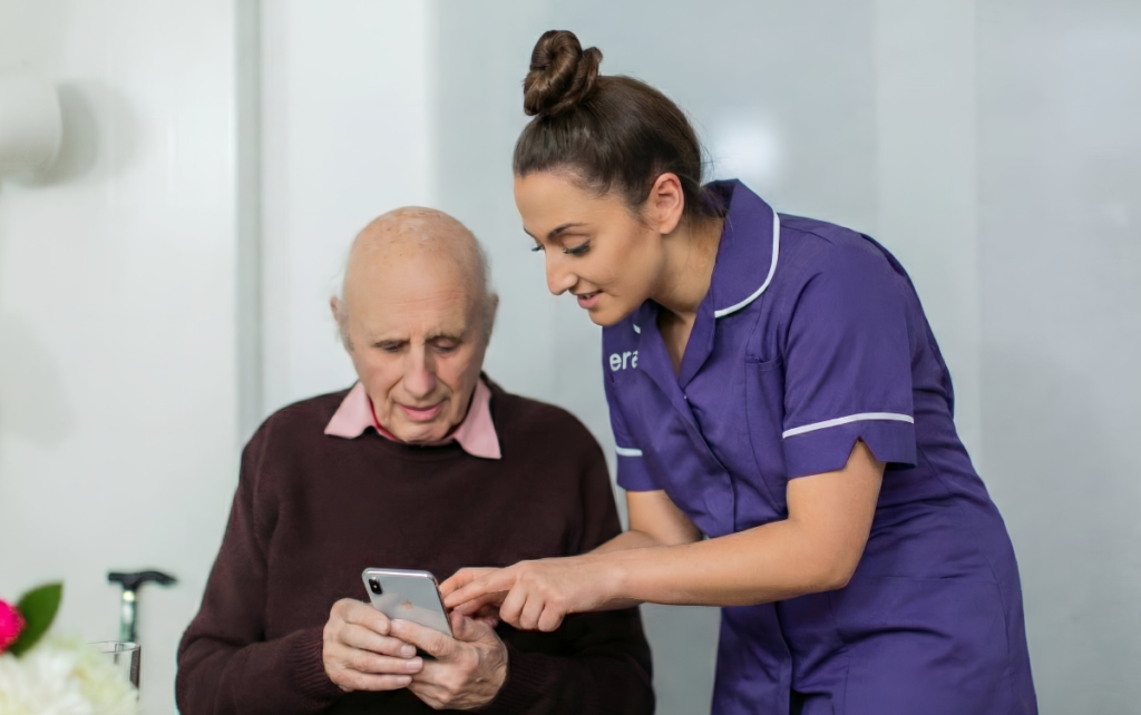 A Cera nurse helping an elderly man use a mobile app during a home healthcare visit to screen for Alzheimer’s clinical trial eligibility.