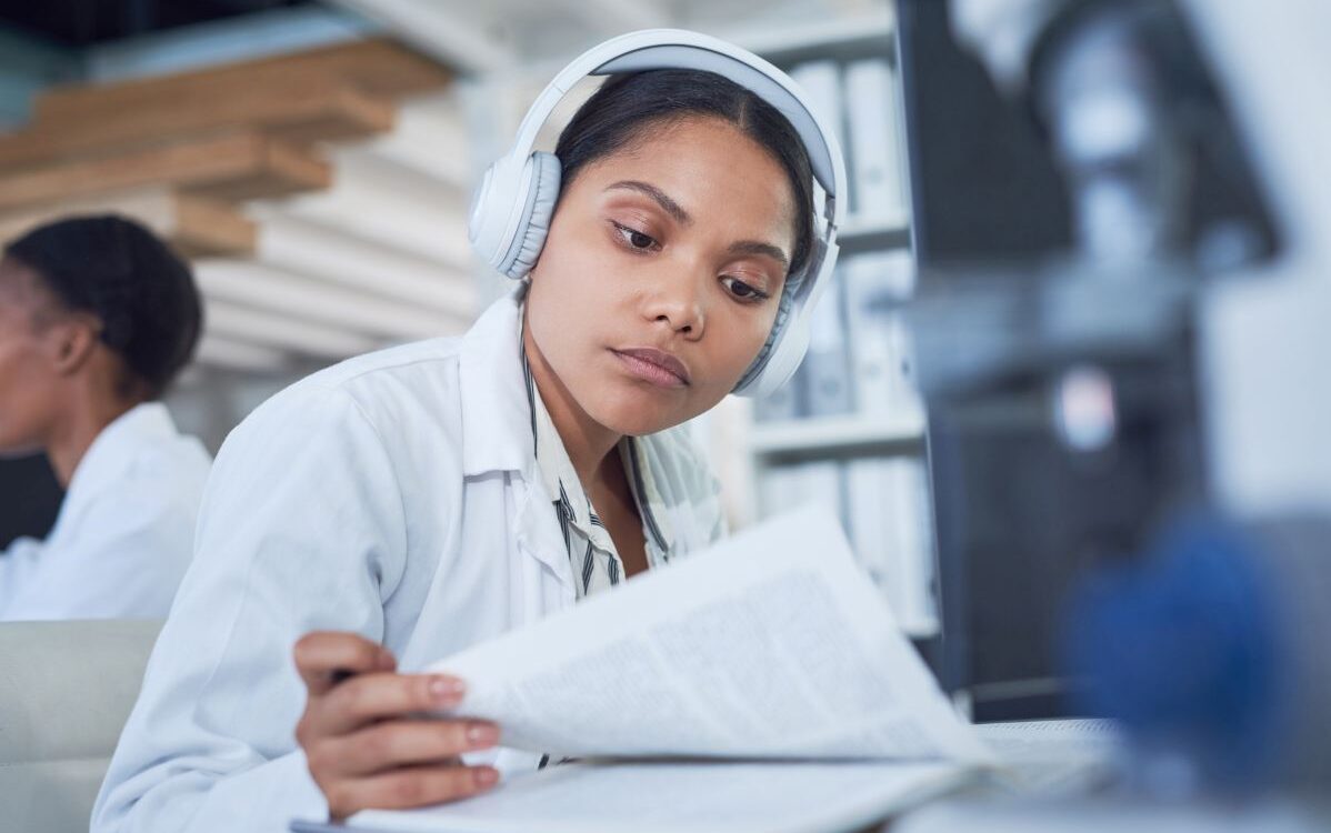 Healthcare professional in lab coat reading medical document with headphones.