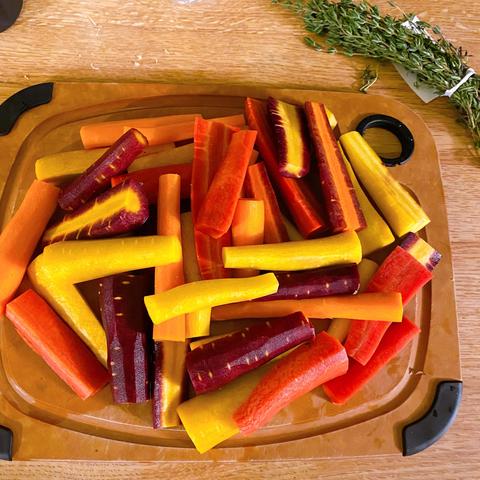 A chopping board with peeled and chopped carrots in orange, yellow, red, and purple. Interestingly, some of the purple ones are yellow inside and some are orange. There's also some fresh thyme that I put on them when they went into the oven