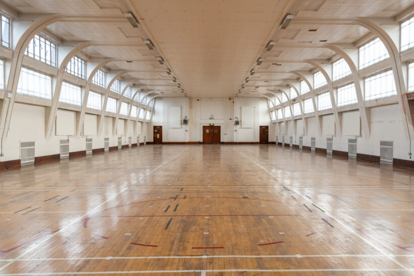 Large sports hall with wooden flooring and markings, on the top floor of the Sackville Street Building in Manchester.