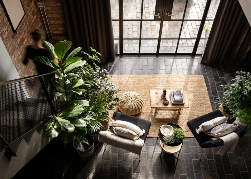 Living room epitomising 2025's 'Biophilic' interior design trend, with a floor to ceiling window, stone floor and lots of plants.